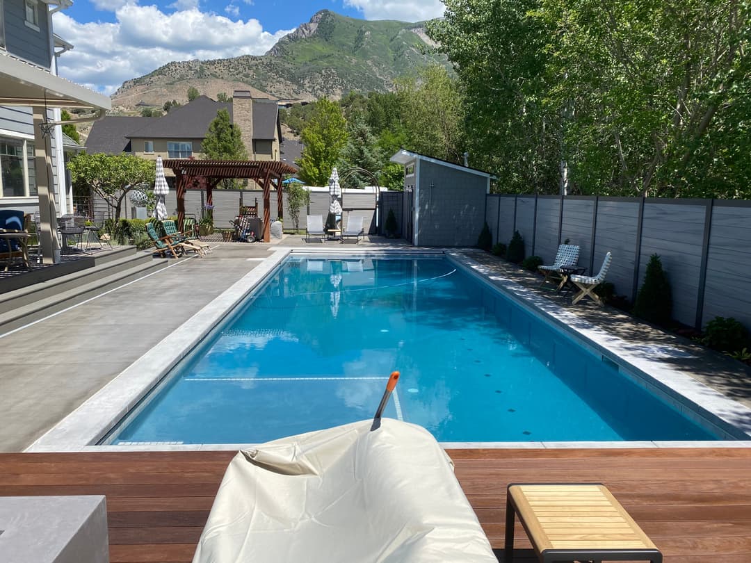 Bright outdoor swimming pool surrounded by trees and mountain views on a sunny day.