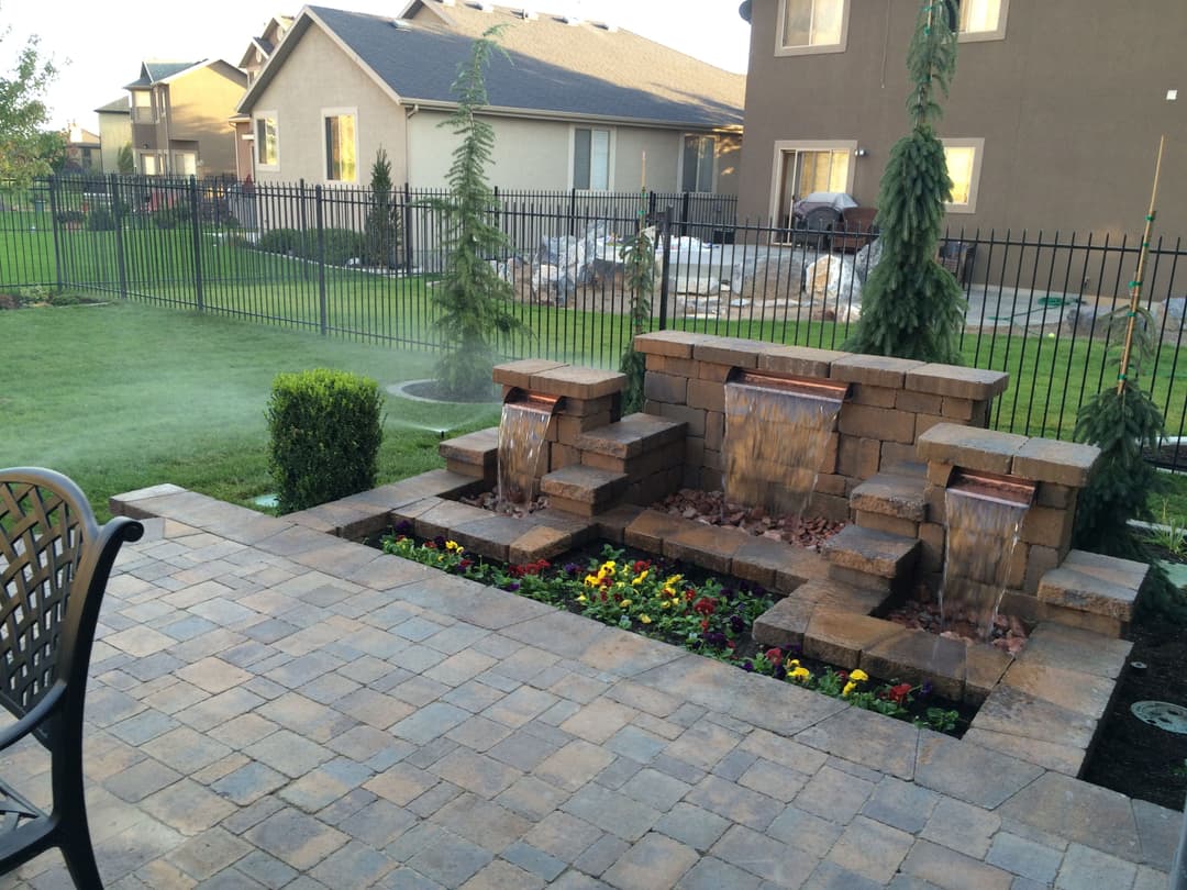 Backyard garden with stone waterfall feature, colorful flowers, and well-maintained lawn.