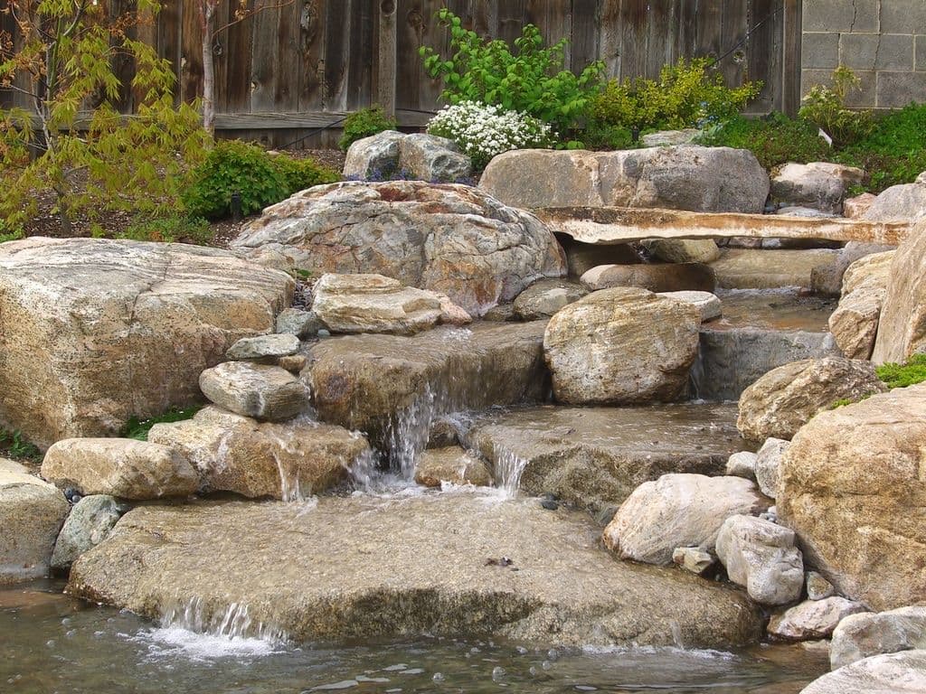 Natural stone waterfall surrounded by lush greenery and textured rocks.