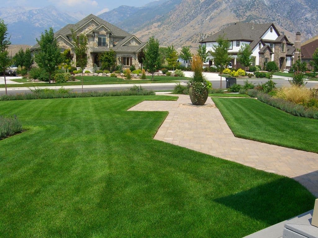 Lush green lawns and landscaped yards in a suburban neighborhood with mountains in background.