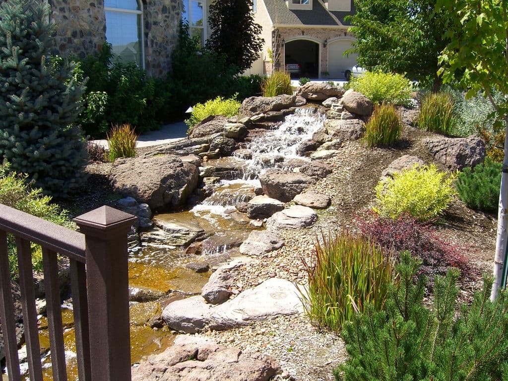 Small outdoor waterfall feature surrounded by lush greenery and stone landscaping.