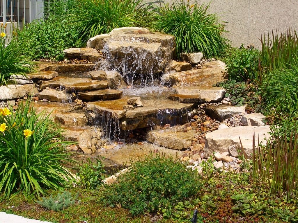 Tranquil stone waterfall surrounded by vibrant greenery and blooming flowers.