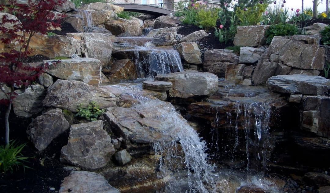 Waterfall flowing over natural stone rocks in a landscaped garden.