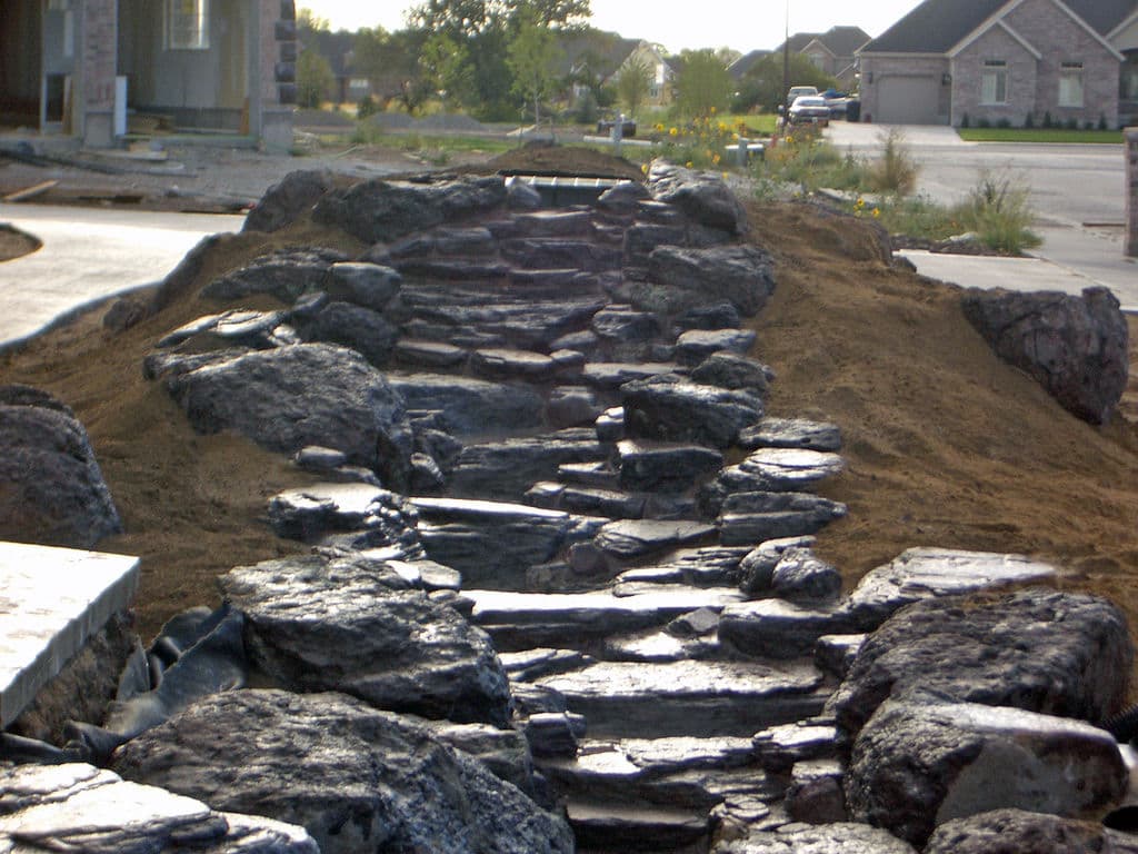 Stone pathway under construction with surrounding earth and landscaping in a residential area.