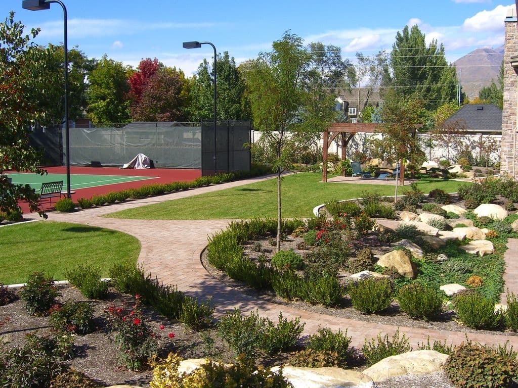 Serene garden path with rocks, colorful trees, and a tennis court in the background.