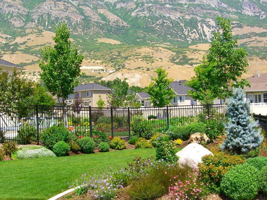 Lush garden with colorful flowers and trees set against a mountain backdrop.