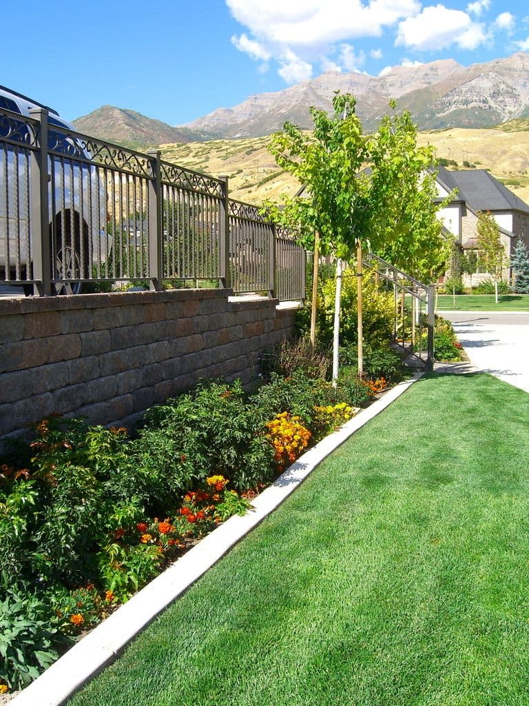 Lush green lawn and vibrant flower beds with mountains in the background and a fence.