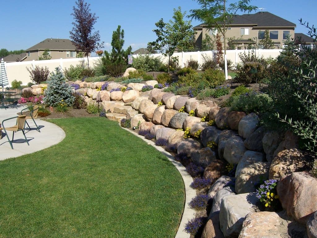 Lush garden landscape with rockery, flowers, and a curved patio in a residential backyard.