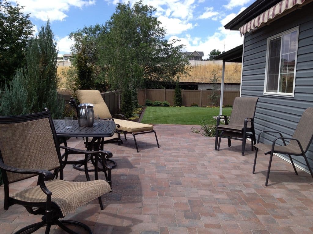 Cozy patio with lounge chairs, dining set, and lush green garden under a blue sky.