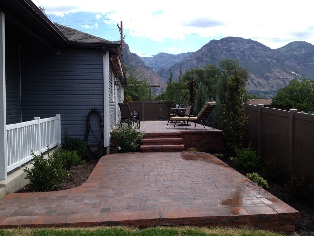 Patio area with stone steps, chairs, and mountains in the background. Lush landscaping visible.