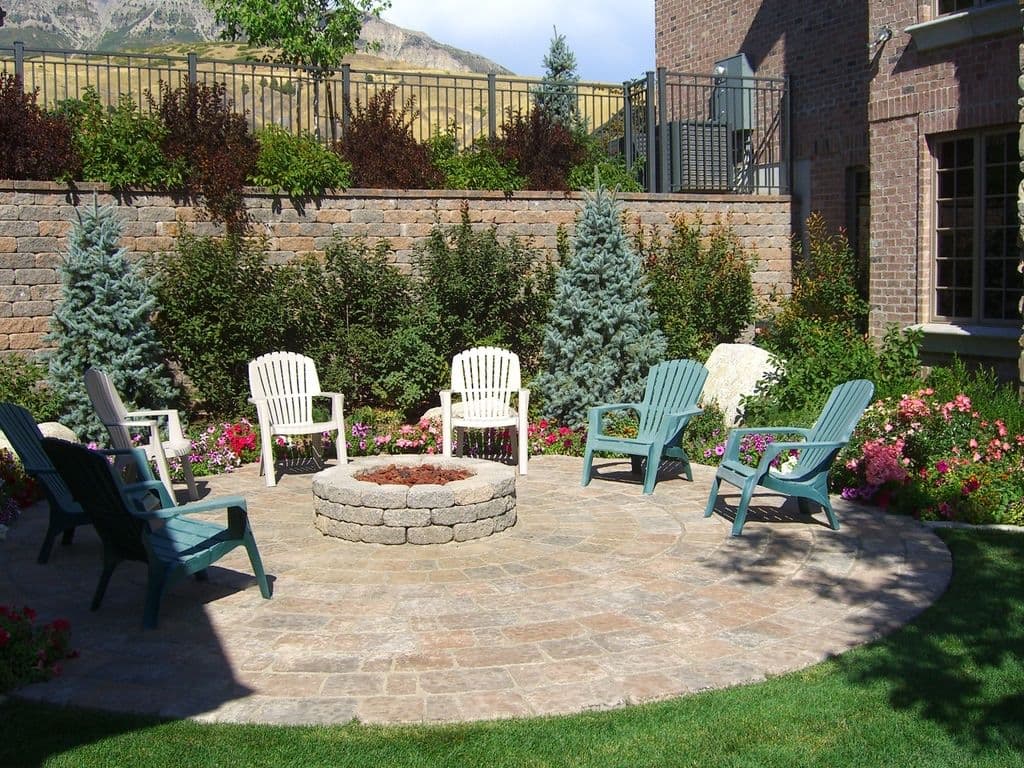 Outdoor patio with stone fire pit surrounded by chairs and colorful flowers.