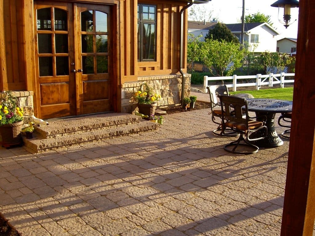 Patio with stone flooring, wooden doors, and potted plants, featuring a dining table and chairs.