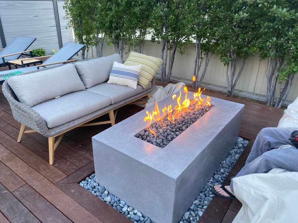 Modern outdoor seating area with a fire pit, surrounded by greenery and wooden decking.