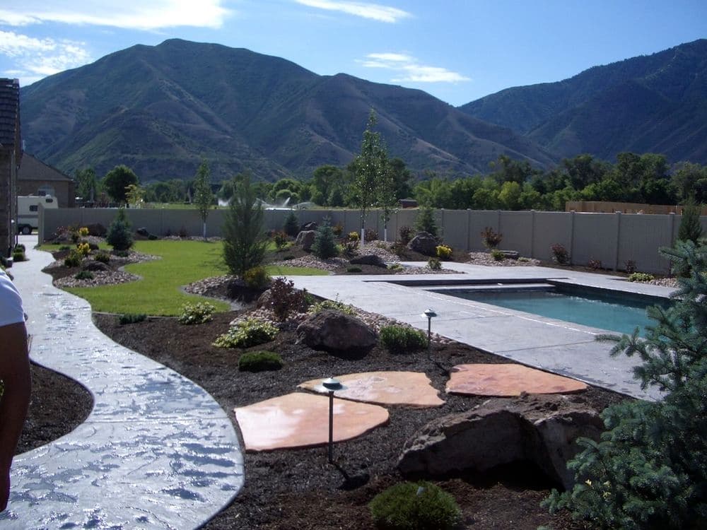 Lush landscape design with pool and mountain backdrop, featuring stone paths and greenery.