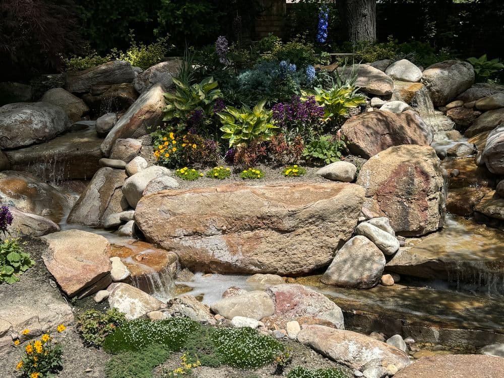 Lush garden waterfall with vibrant flowers and cascading water over rocks.