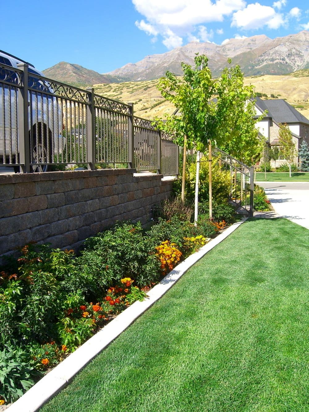Lush garden with colorful flowers, trimmed grass, and mountains in the background.